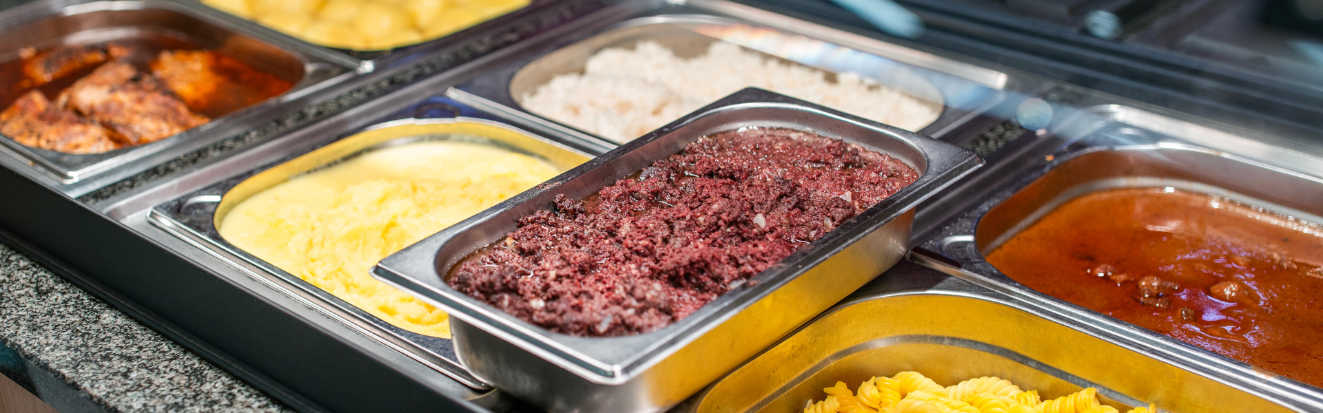 Heißtheke im Supermarkt mit mehreren GN-Behältern – u. a. Nudeln, Kartoffeln, Beilagen und Soßen.
