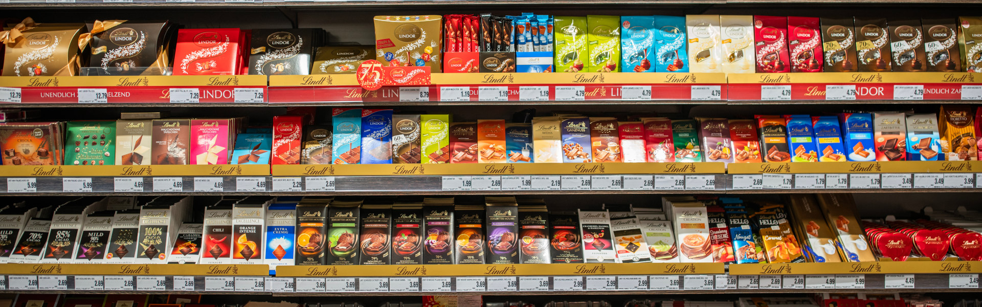 Regal mit vielfältiger Lindt-Schokolade – Tafeln, Pralinen und Lindor-Produkten, frontal aufgenommen.