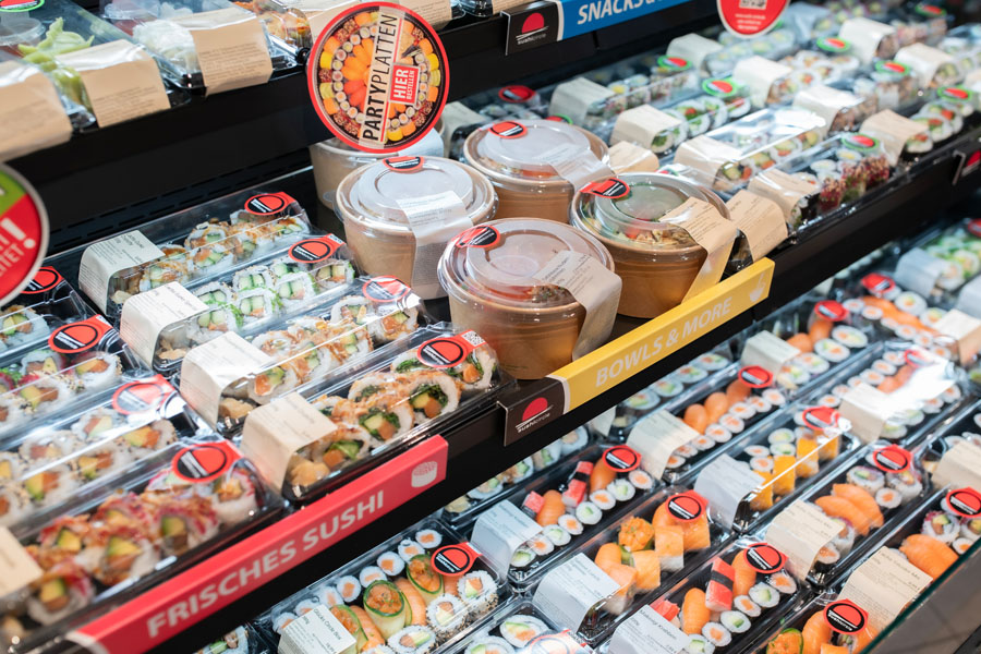 Kühltheke mit frischem Sushi und Bowls in To-Go-Verpackungen, verschiedene Sorten in Reihen.